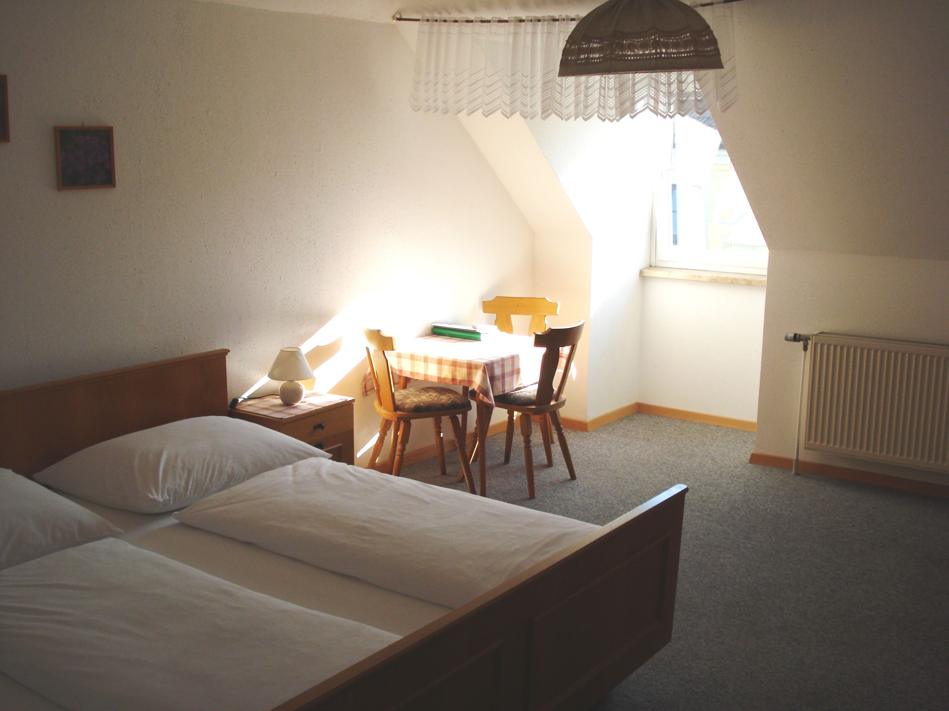 Ein einfach eingerichtetes Zimmer mit Bett, Tisch, Stühlen und Fenster.