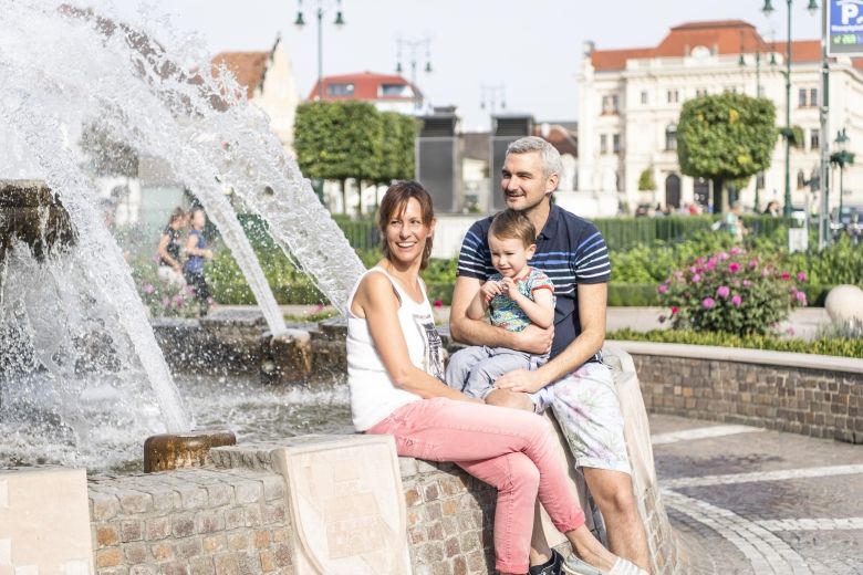 Eine Familie sitzt lächelnd an einem Brunnen auf dem Tullner Hauptplatz.