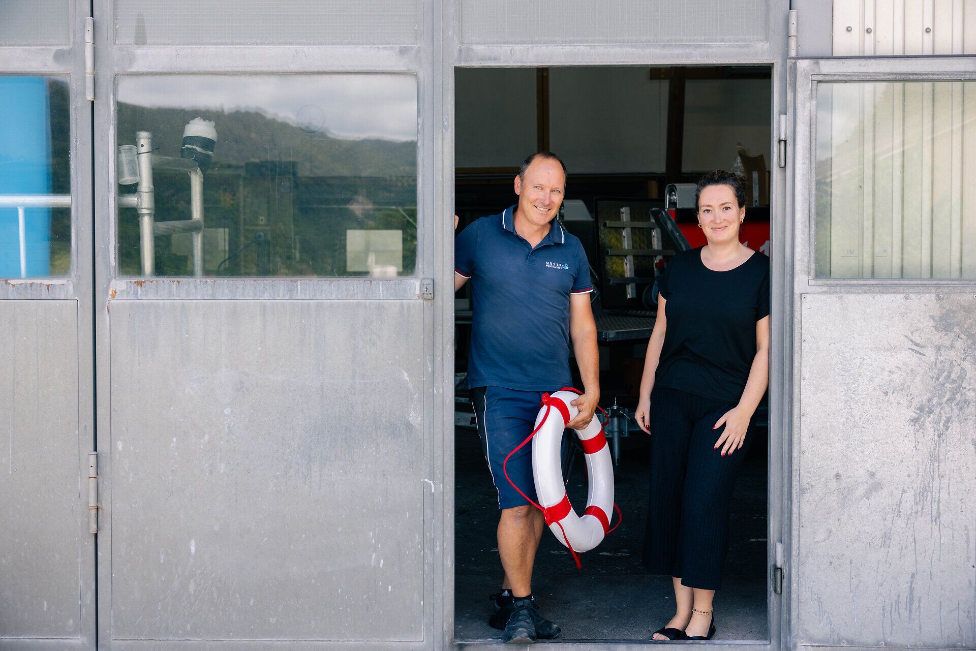 Ein Mann und eine Frau vor dem Eingang der Schiffswerft mit einem Rettungsring.