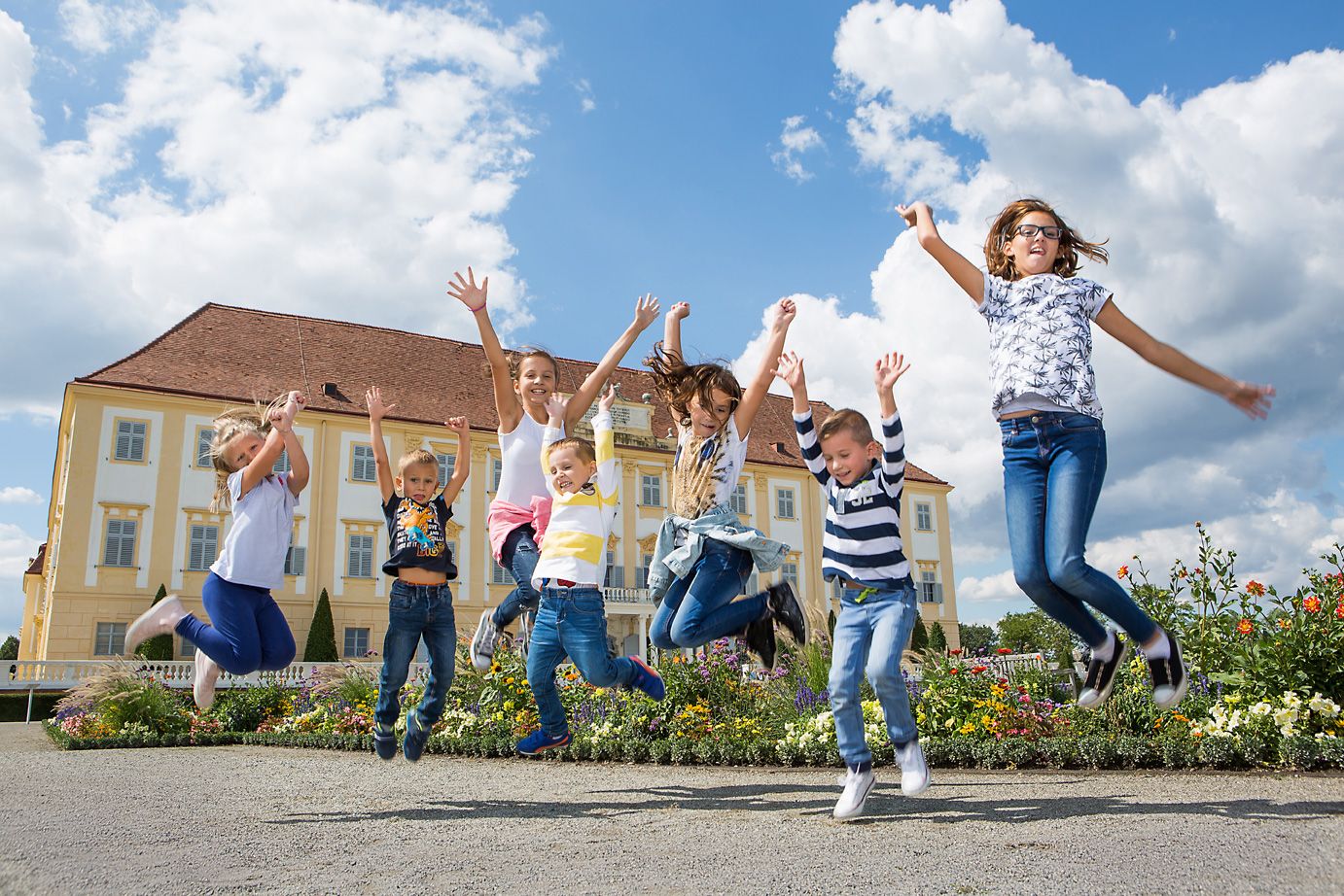 Mehrere Kinder springen in die Luft. Im Hintergrund Schloss Hof 