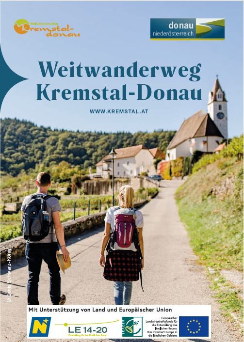 Ein Mann und eine Frau gehen auf einem asphaltiertem Weg in die Richtung einer Kirche.