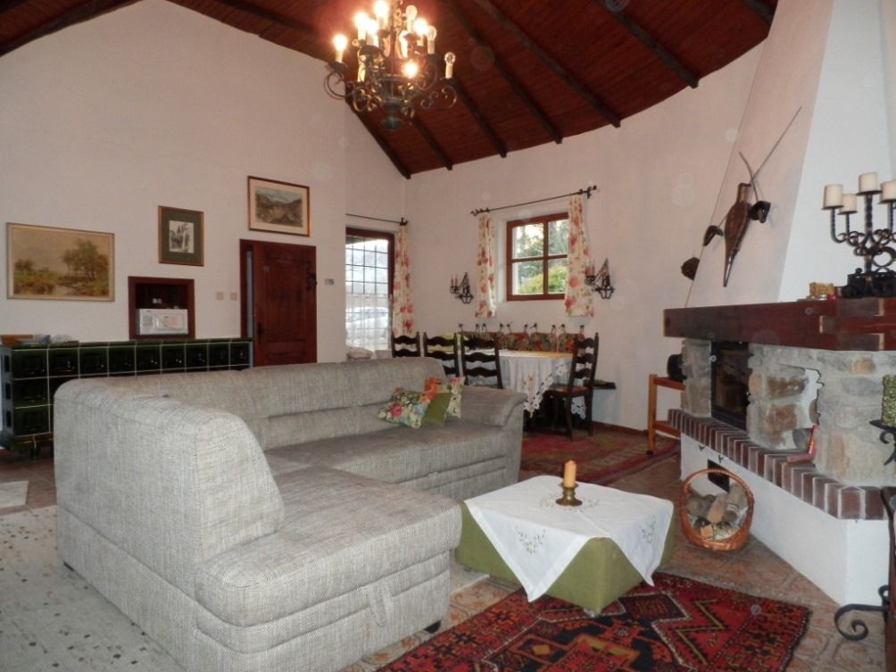 Gemütliches Wohnzimmer mit grauem Sofa, Kamin und Esstisch. Rustikale Dekoration und Holzbalkendecke.