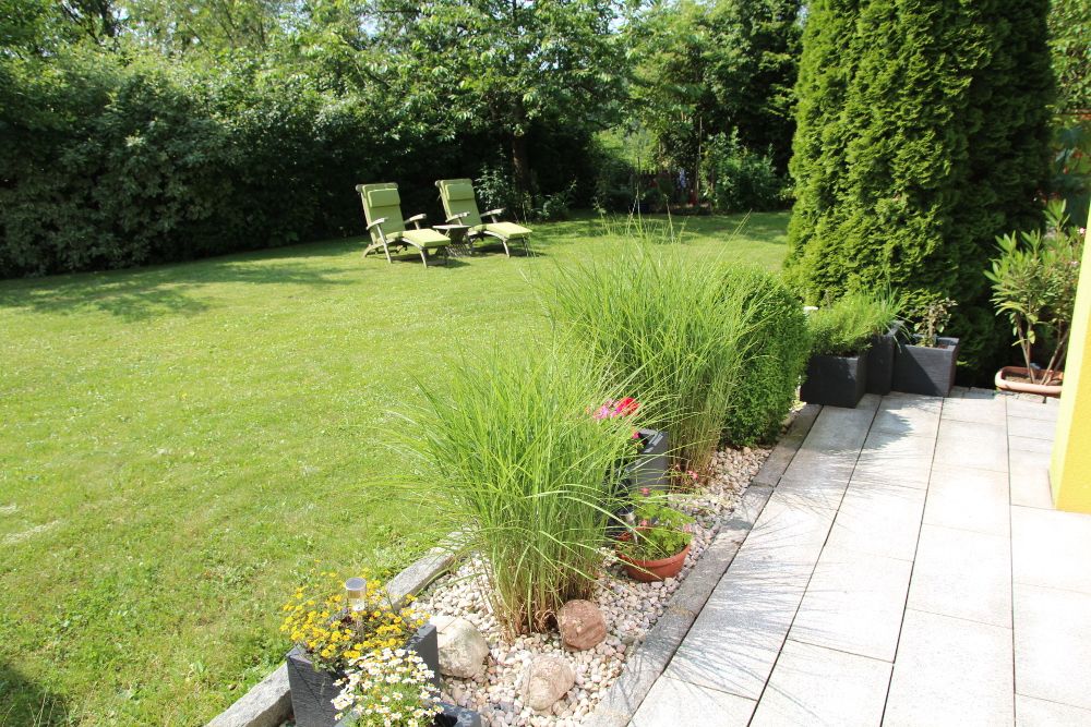 Garten mit Rasenfläche, Liegestühlen und bepflanztem Rand.