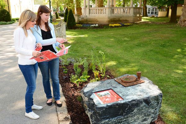 Zwei Frauen betrachten Informationsmaterial an einem Stein mit einer Gedenktafel im Freien.
