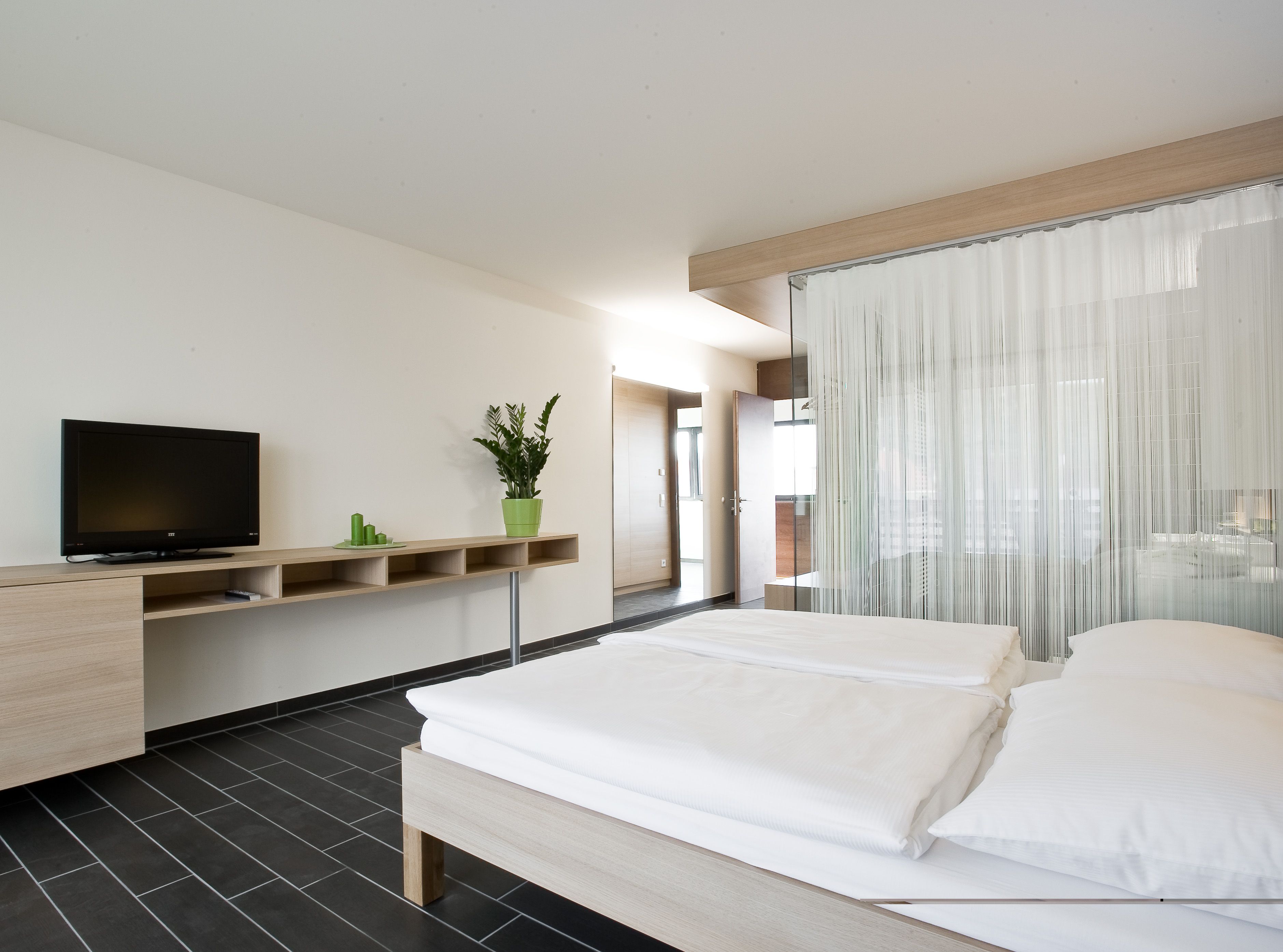 Modernes Hotelzimmer mit Doppelbett, Fernseher und Pflanzen.