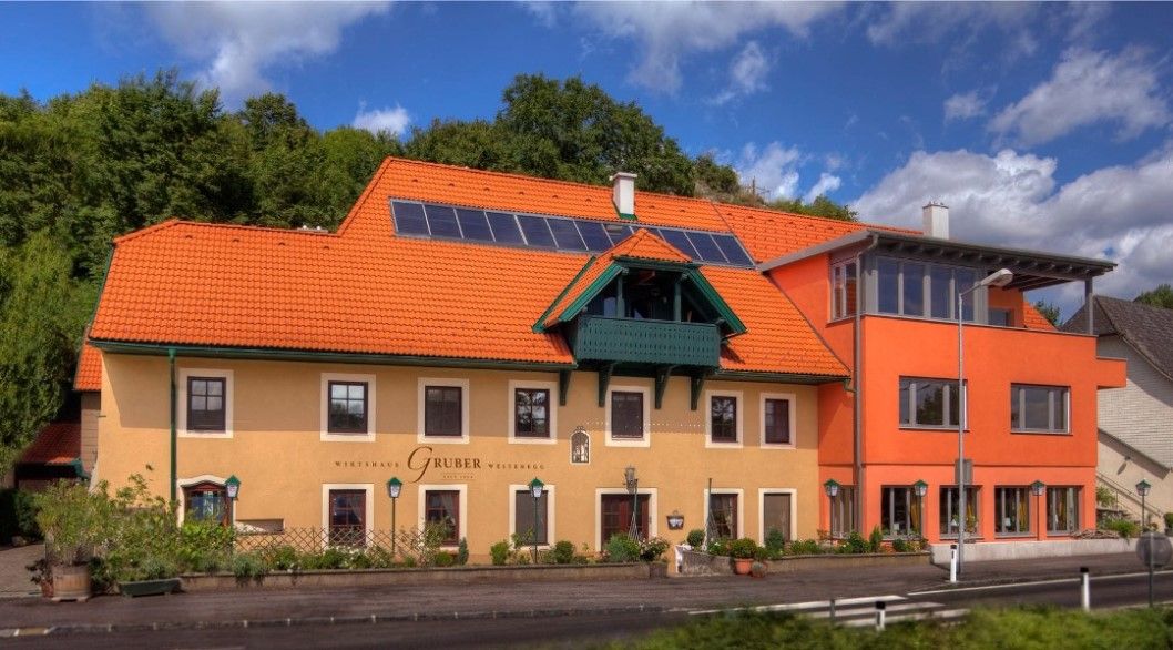 Ein traditionelles Wirtshaus mit orangefarbenem Dach und Solarpanelen, umgeben von grüner Natur.