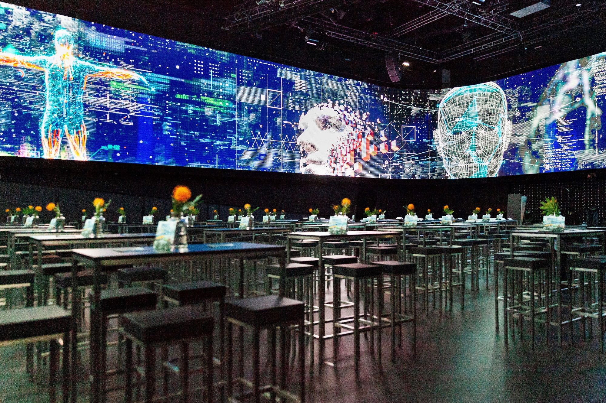 A modern showroom with digital projections and tables with flowers.