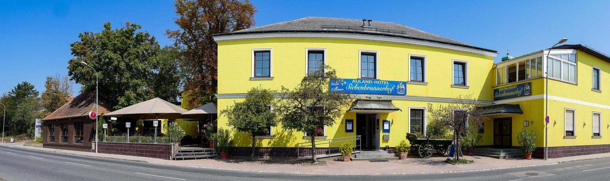 Sárga épület étteremmel és szállodával, fákkal és úttal körülvéve.