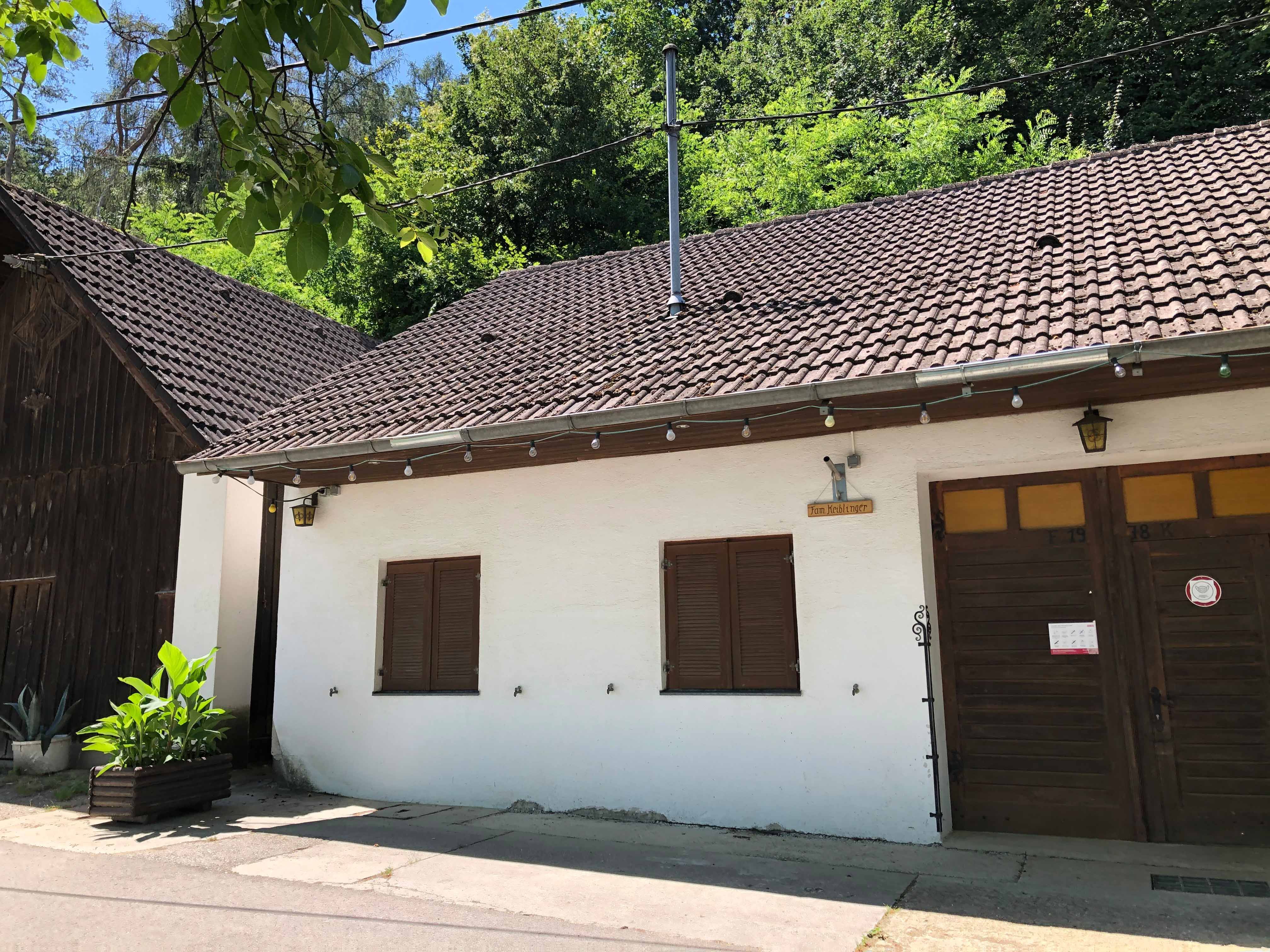 Außenansicht eines Heurigenlokals mit weißer Fassade und Holztor.