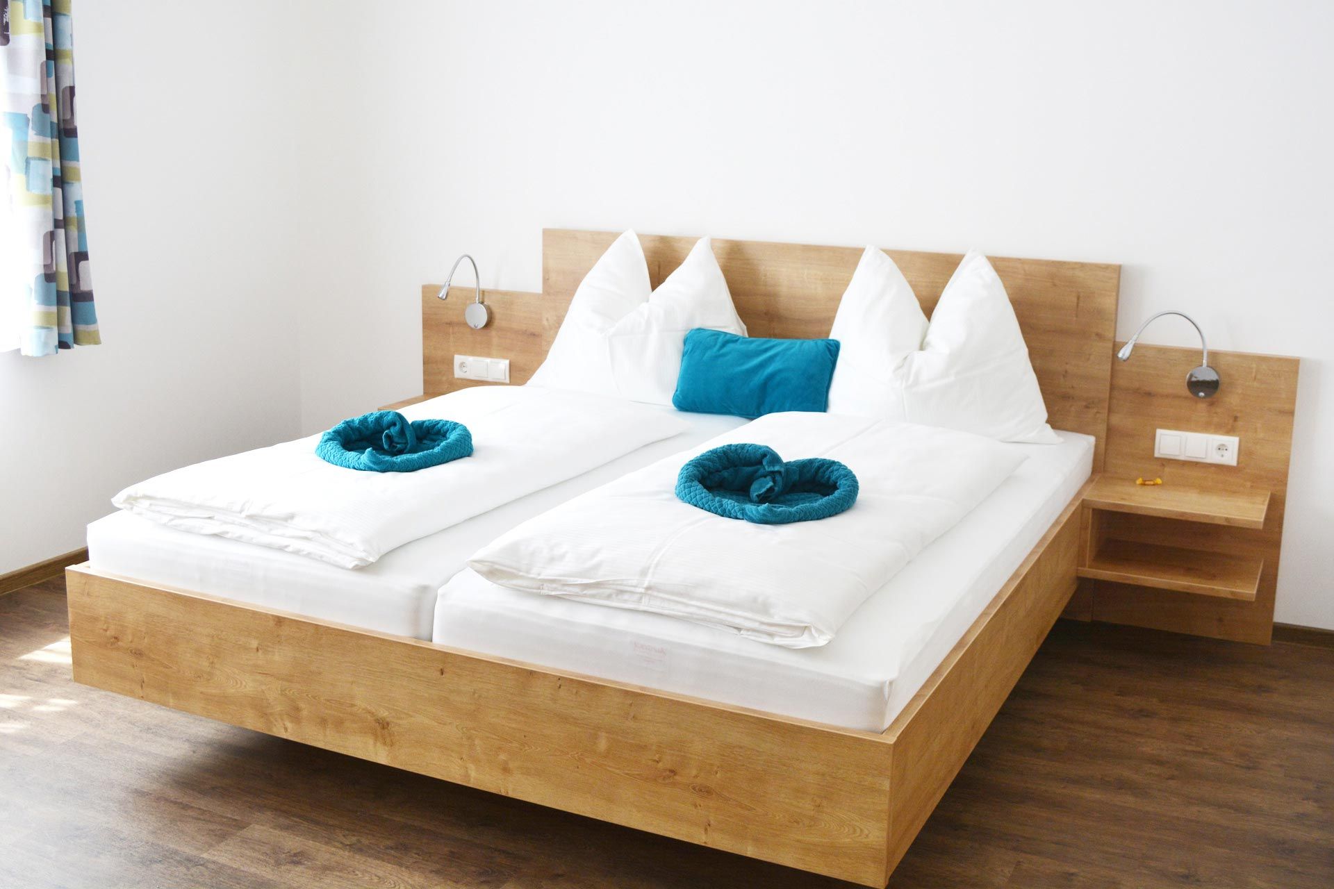 Modernes Gästezimmer mit Doppelbett, weißen Bettdecken und blauen Kissen.