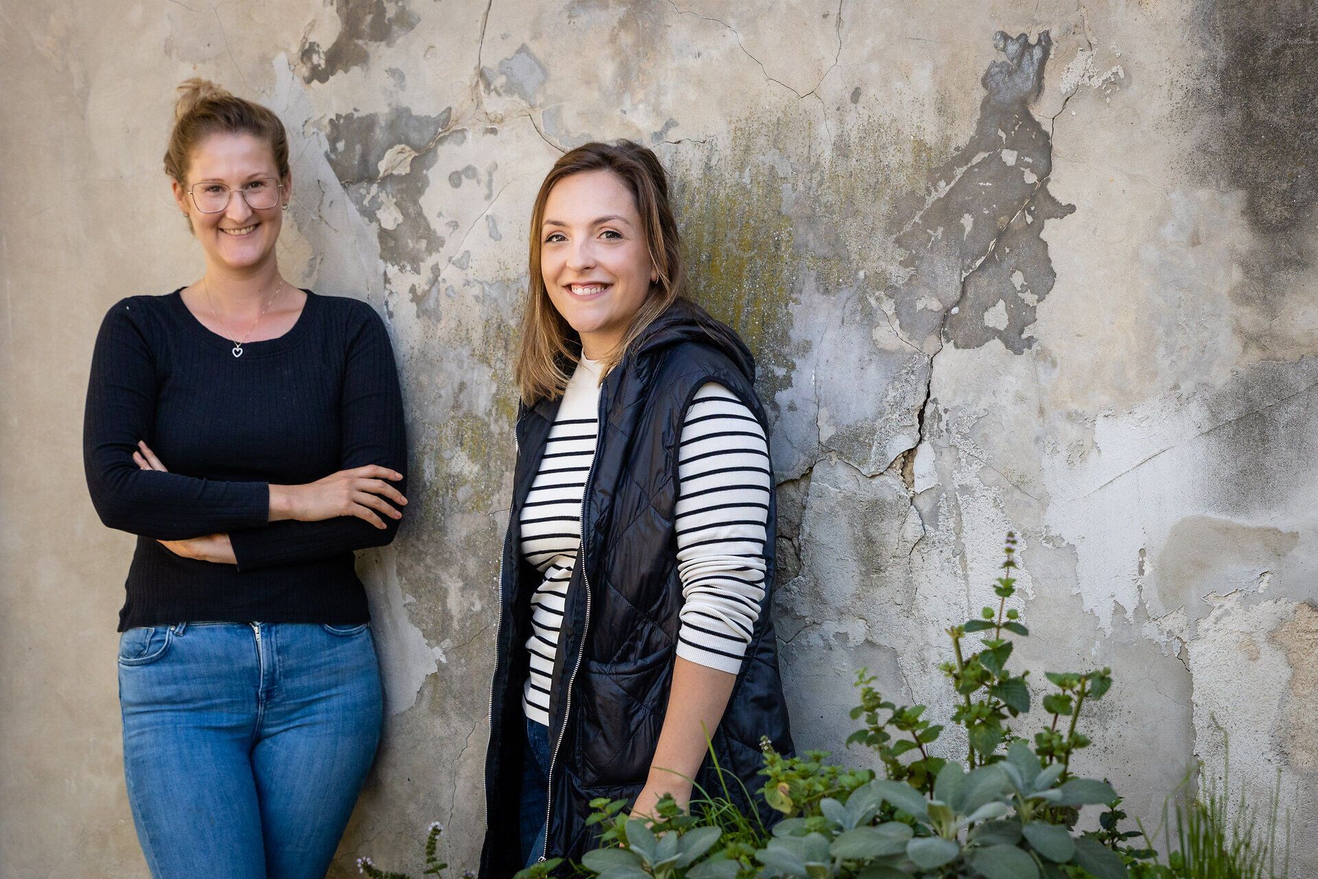 Die Winzerinnen Stefanie Böheim und Michaela Riedmüller lehnen an einer Wand.