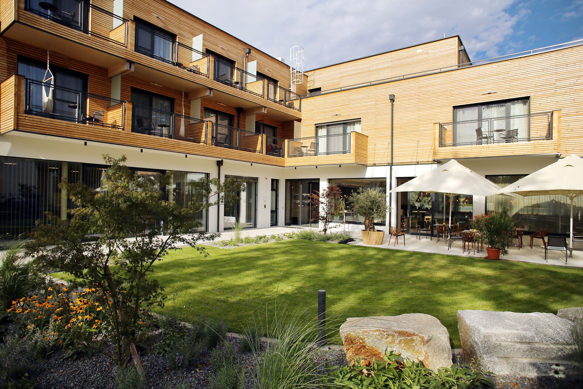Umgeben von einer malerischen Gartenlandschaft lädt die Donau Lodge Ybbs zu entspannenden Stunden ein. Die harmonische Architektur und die blühenden Pflanzen schaffen eine einladende Atmosphäre, die zum Verweilen einlädt.