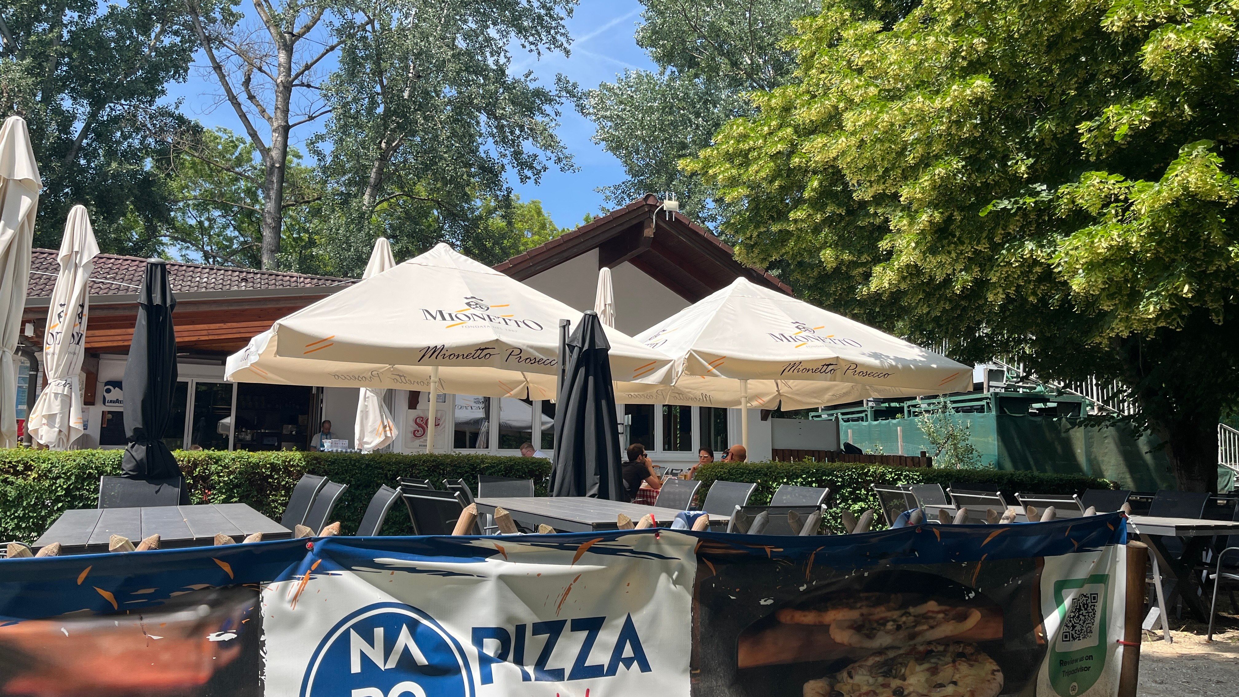 Gastgarten mit Blick auf das Gebäude der Pizzeria, im Hintergrund Bäume.
