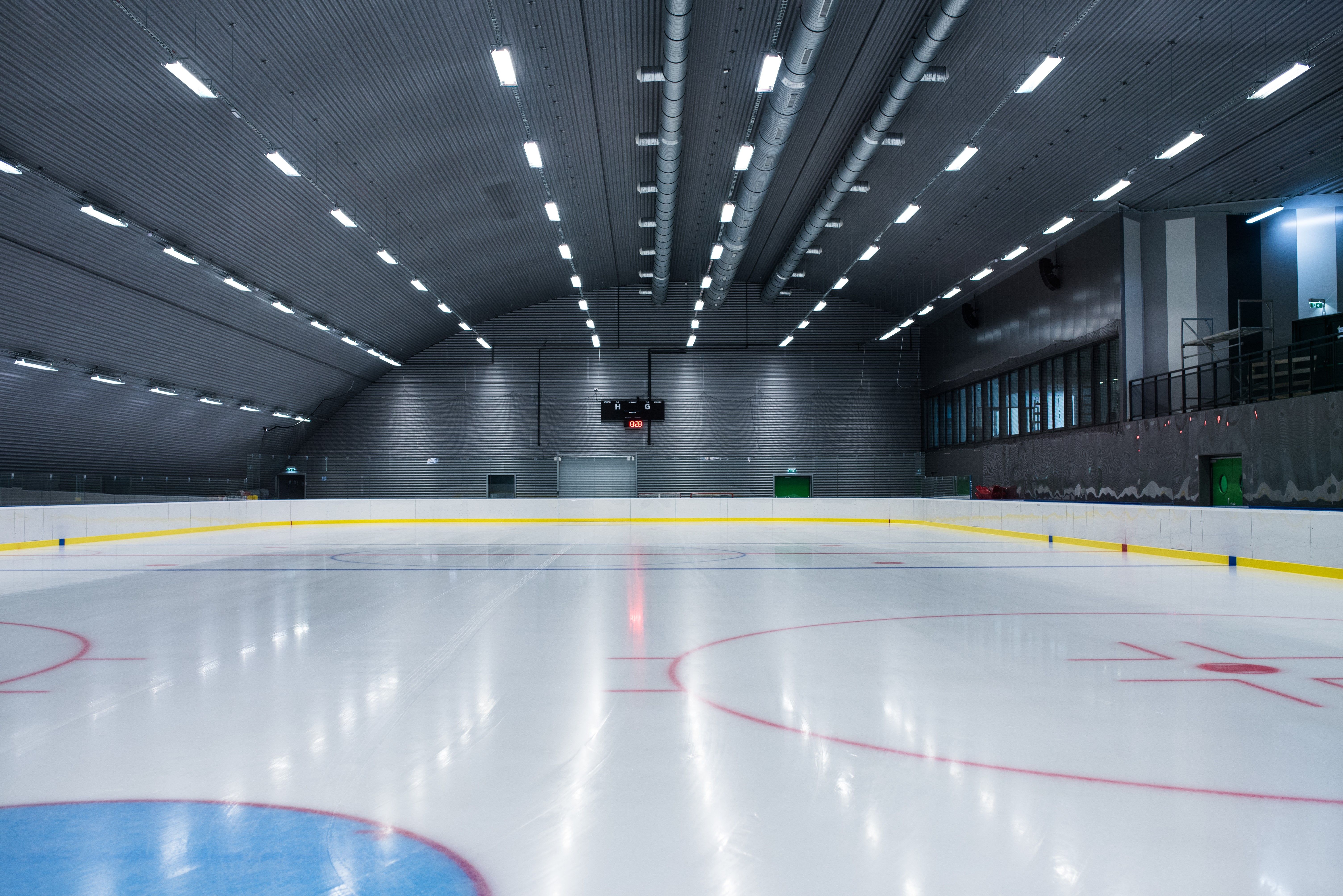 Leere Eishalle mit beleuchtetem Spielfeld und Anzeigetafel.