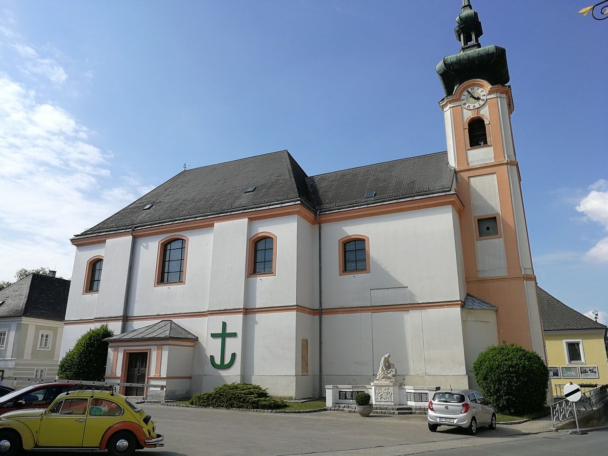 Pfarrkirche Würmla mit Uhrturm und parkenden Autos.