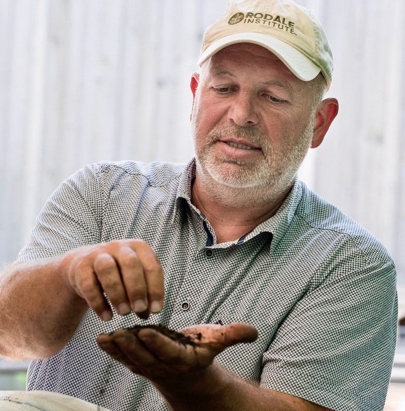 Mann hält Erde in der Hand und lässt sie prüfend durch die Finger rieseln.