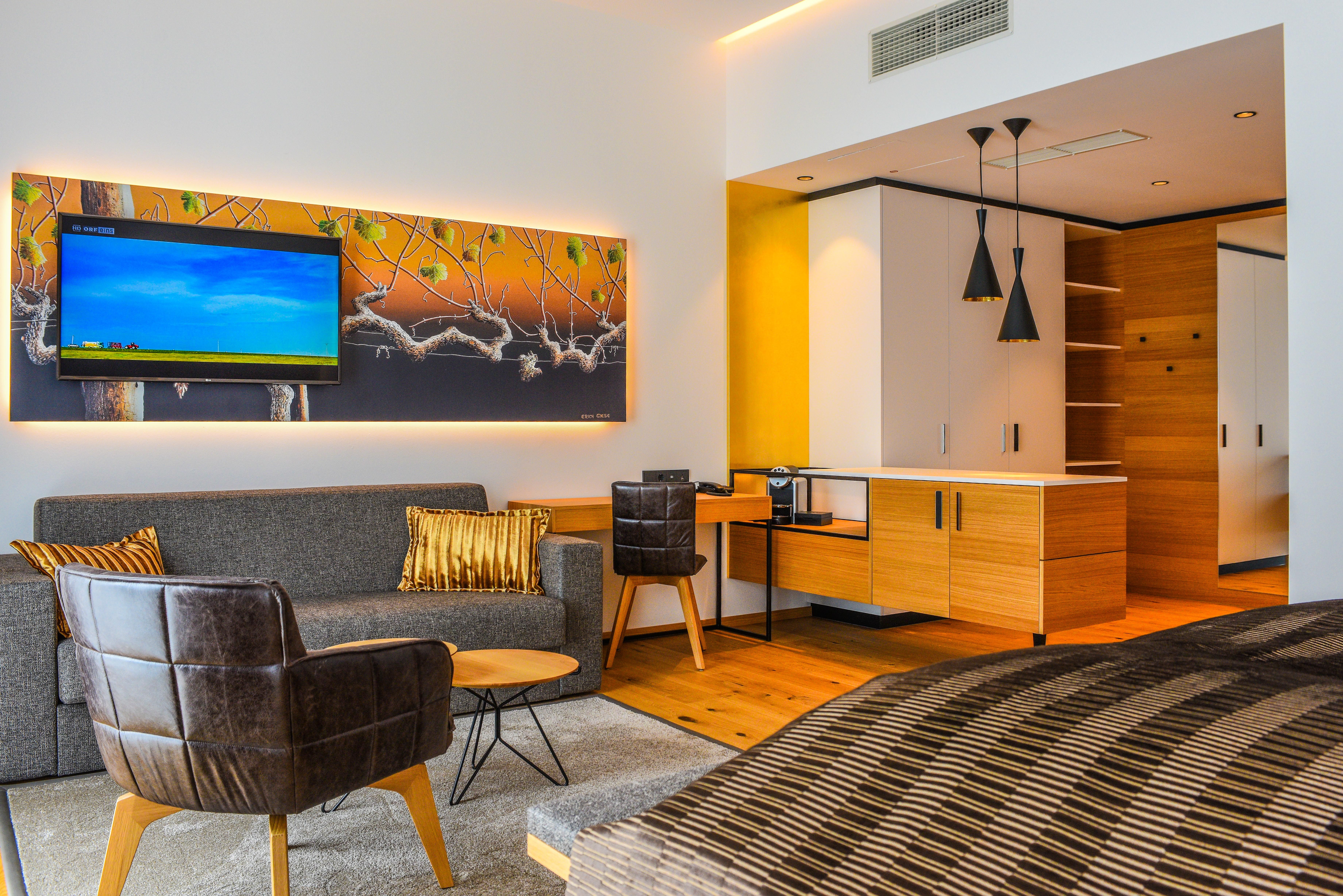 Moderne Hotelsuite mit Sofa, Sessel, TV und Küchenzeile.