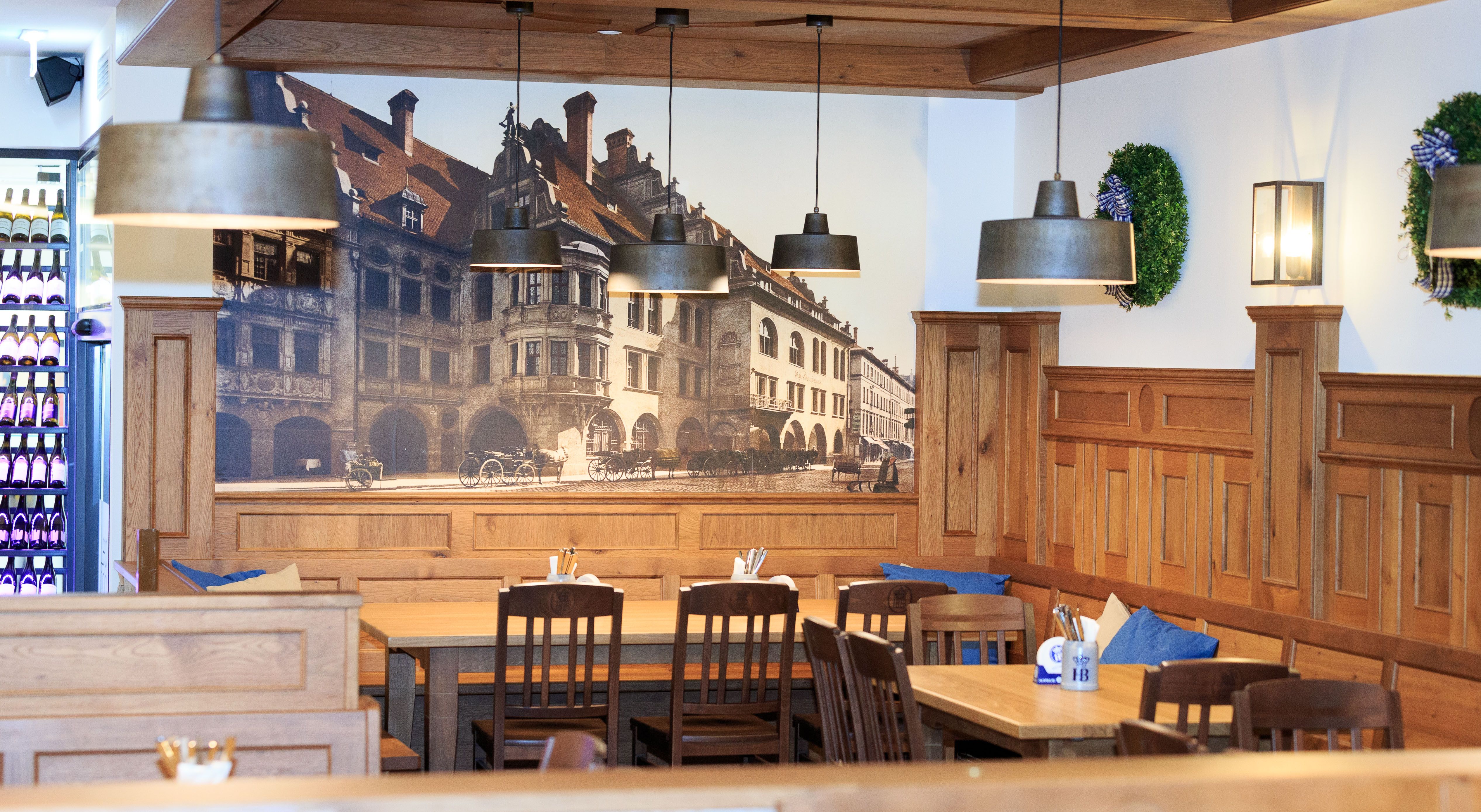 Innenansicht eines traditionellen bayerischen Restaurants mit Holzmöbeln und Wandbild des Hofbräuhauses.