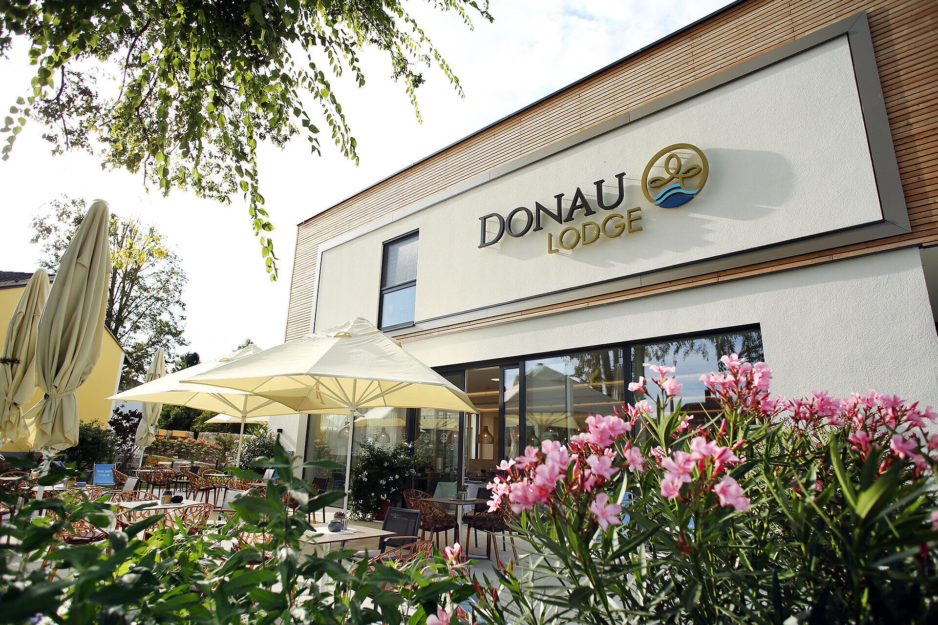 Die Donau Lodge Ybbs strahlt eine einladende Atmosphäre aus, umgeben von blühenden Pflanzen und einem malerischen Blick auf den Fluss. Hier können Besucher die Ruhe der Natur genießen und sich auf eine entspannte Auszeit freuen.