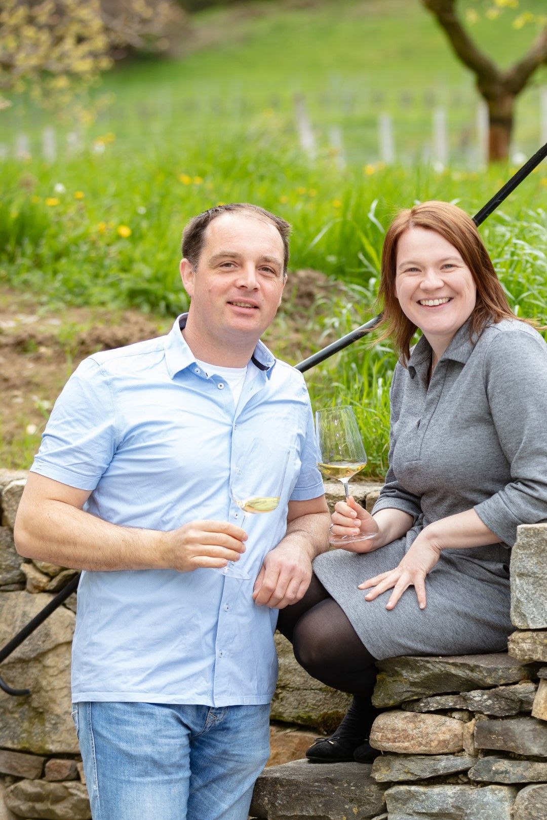 Ein Mann und eine Frau sitzen auf einer Steinmauer im Freien und halten Weingläser in der Hand.
