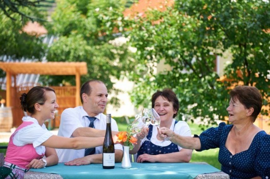 Vier Personen stoßen im Freien mit Weingläsern an einem Tisch an.