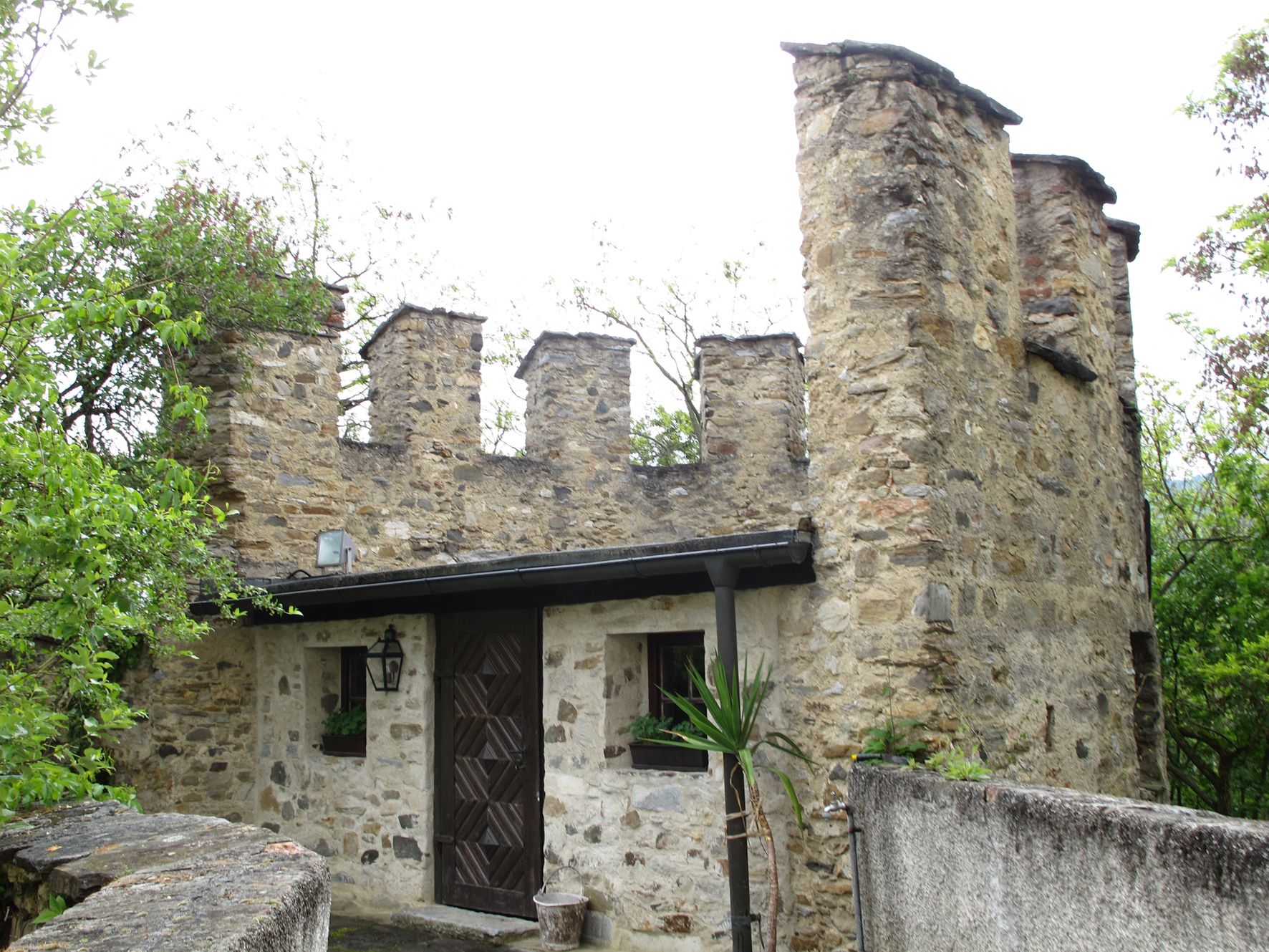 Stone wall with battlements and door, surrounded by trees.