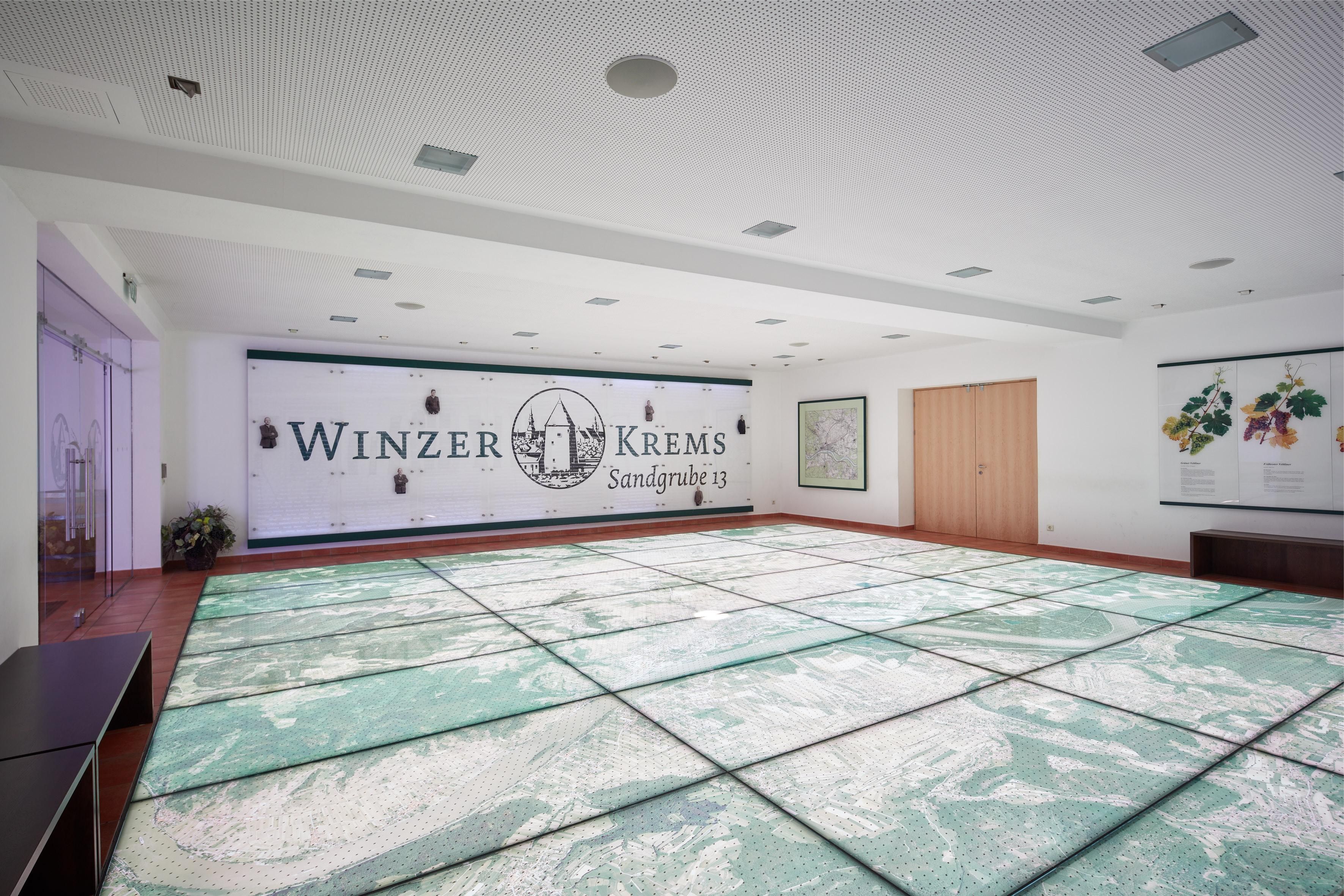 Ein großer Raum mit einem hellen Fußboden, der die Riedenkarte zeigt, im Hintergrund eine große Tafel mit dem Schriftzug Winzer Krems.