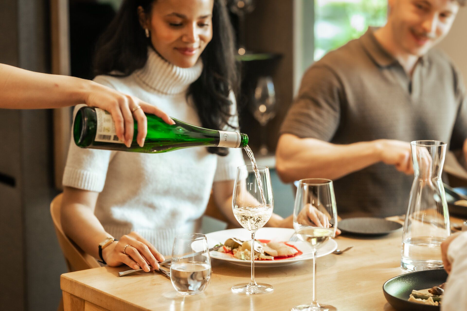 Beim gemeinsamen Essen wird Wein in ein Glas eingeschenkt.