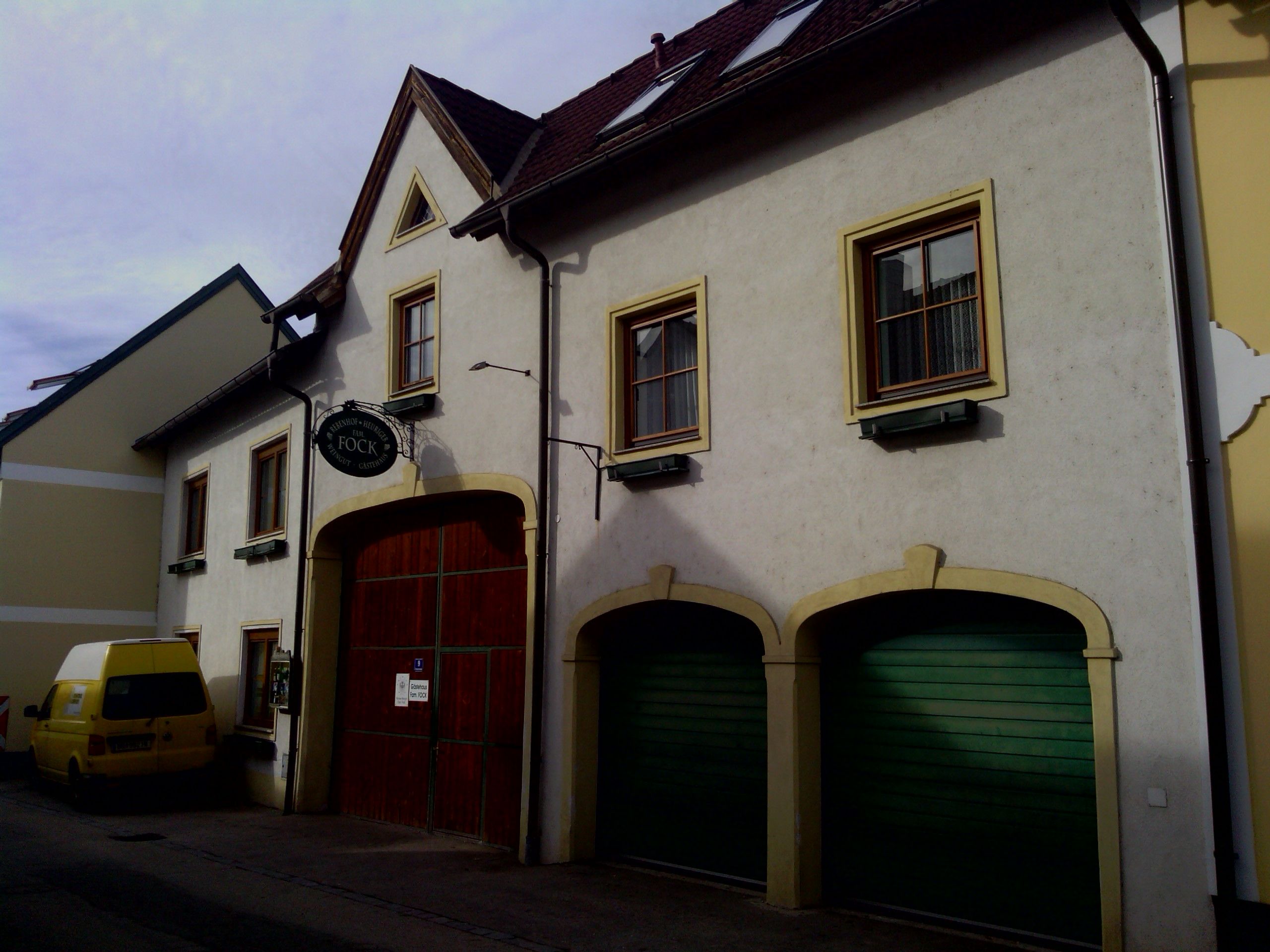 Außenansicht eines Gebäudes mit gelbem Van und grünen Garagentoren.