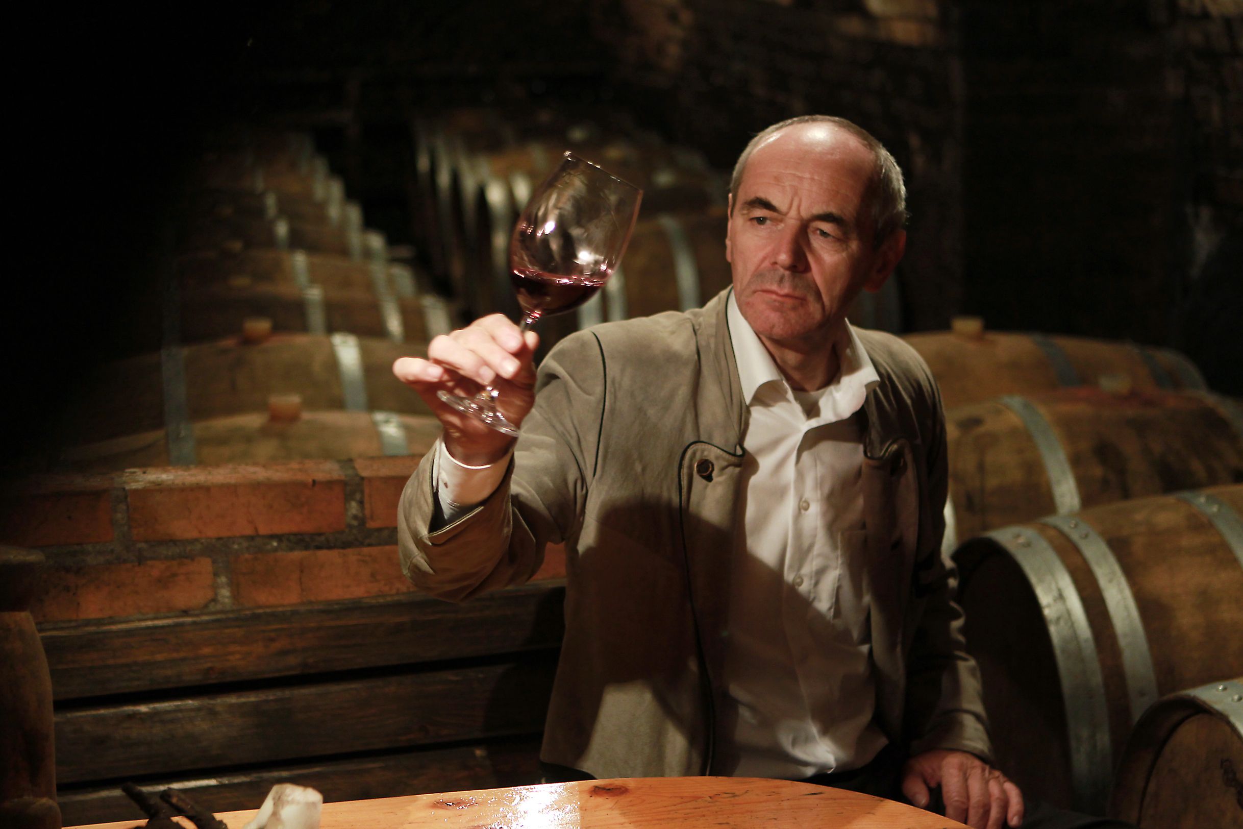 Ein Mann im Weinkeller hält ein Glas Rotwein hoch.