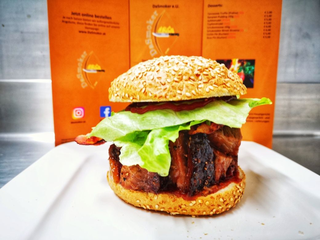 Ein Burger mit Salat und Fleisch auf einem weißen Teller vor einer orangefarbenen Speisekarte.