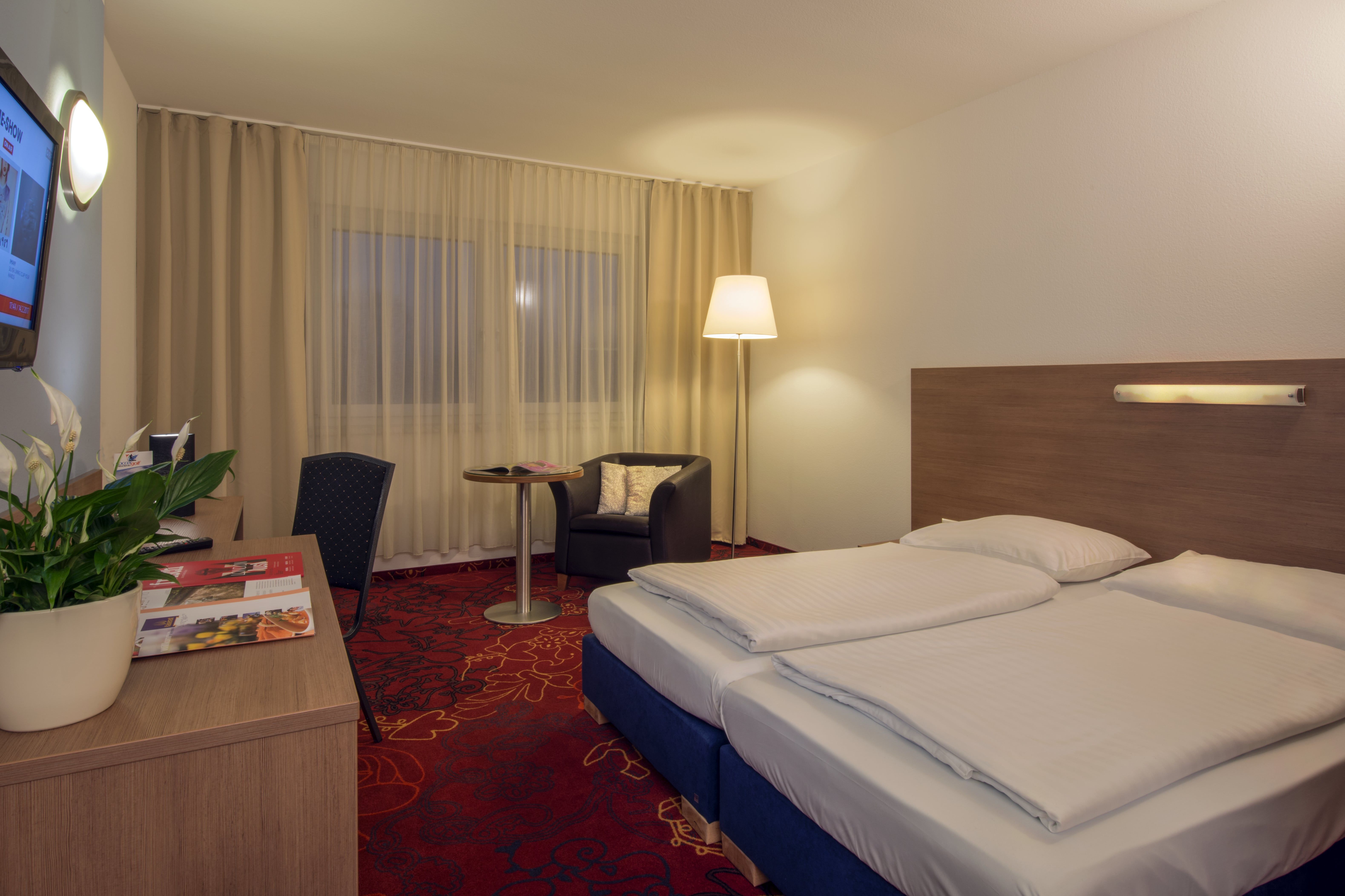 Doppelzimmer mit rotem Teppichboden, Schreibtisch und großem Doppelbett.