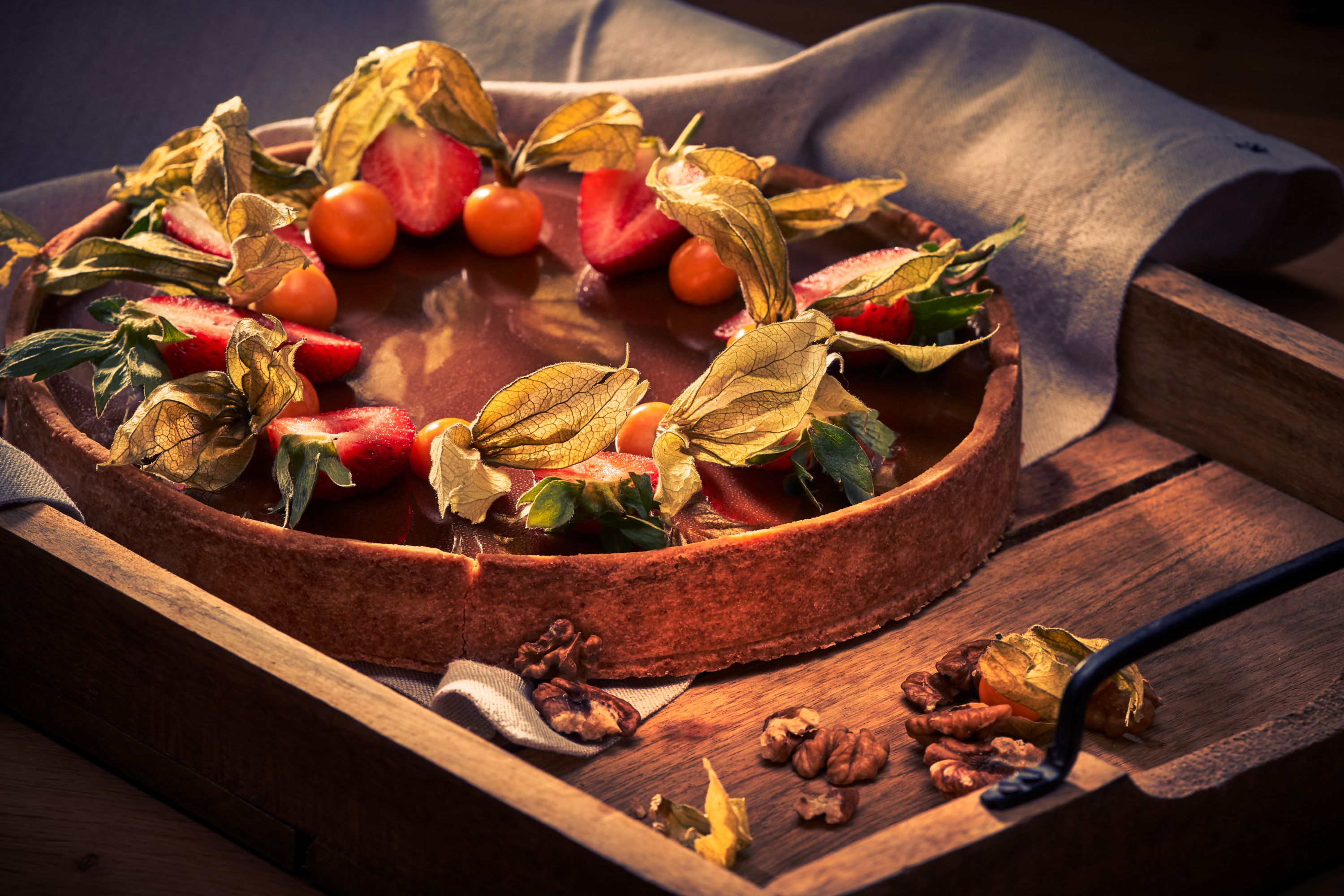 Eine Torte mit Schokoladenglasur, dekoriert mit Erdbeeren und Physalis, auf einem Holztablett.
