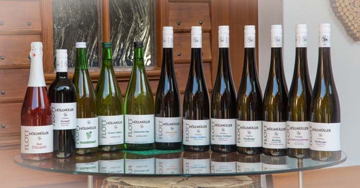 Eine Auswahl von Weinflaschen auf einem Glastisch vor einer Holzwand.