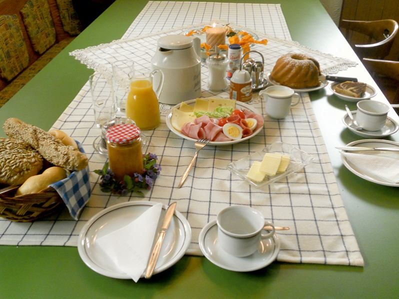 Ein gedeckter Frühstückstisch mit Brötchen, Aufschnitt, Käse, Saft, Kaffee und Kuchen.