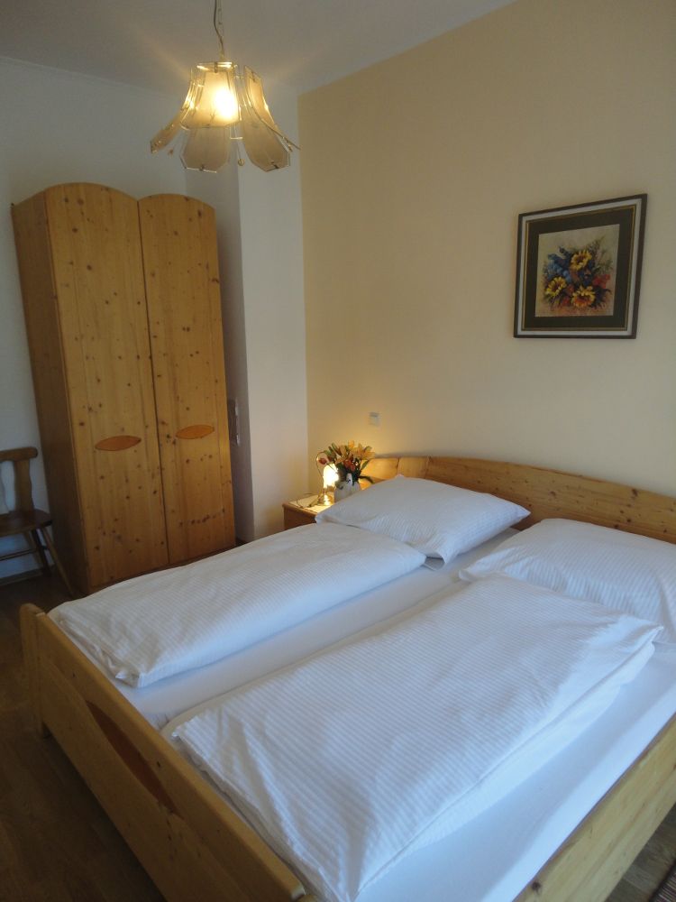 Ein gemütliches Schlafzimmer mit Doppelbett, Holzschrank, Nachttisch mit Blumen und einem Gemälde an der Wand.