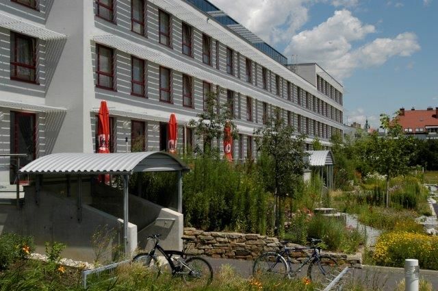 Modernes Gebäude mit mehreren Stockwerken, umgeben von grüner Landschaft und Fahrrädern im Vordergrund.