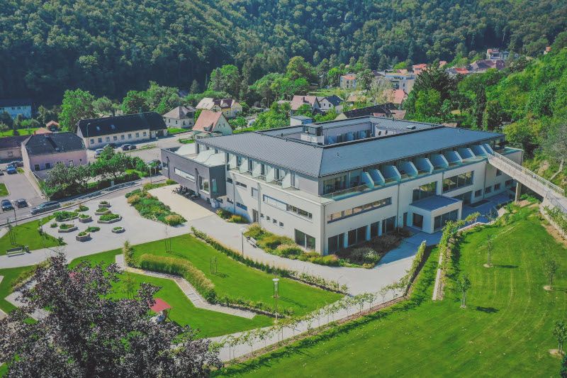 Luftaufnahme eines modernen Gebäudes mit Garten und umliegender Landschaft.