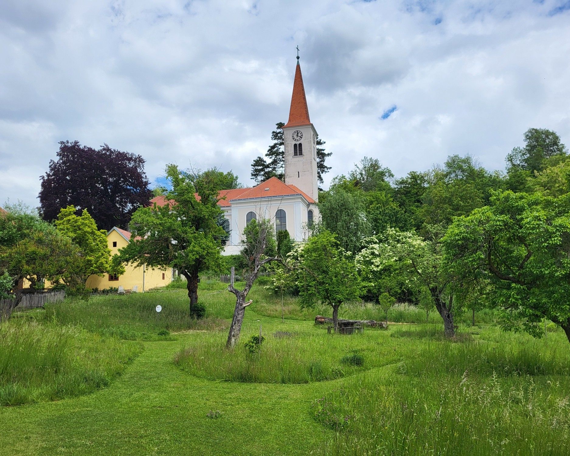 Pfarrgarten in Königsbrunn am Wagram mit Blick auf die historische Kirche, umgeben von grünen Wiesen, alten Obstbäumen und naturnaher Gartenlandschaft.