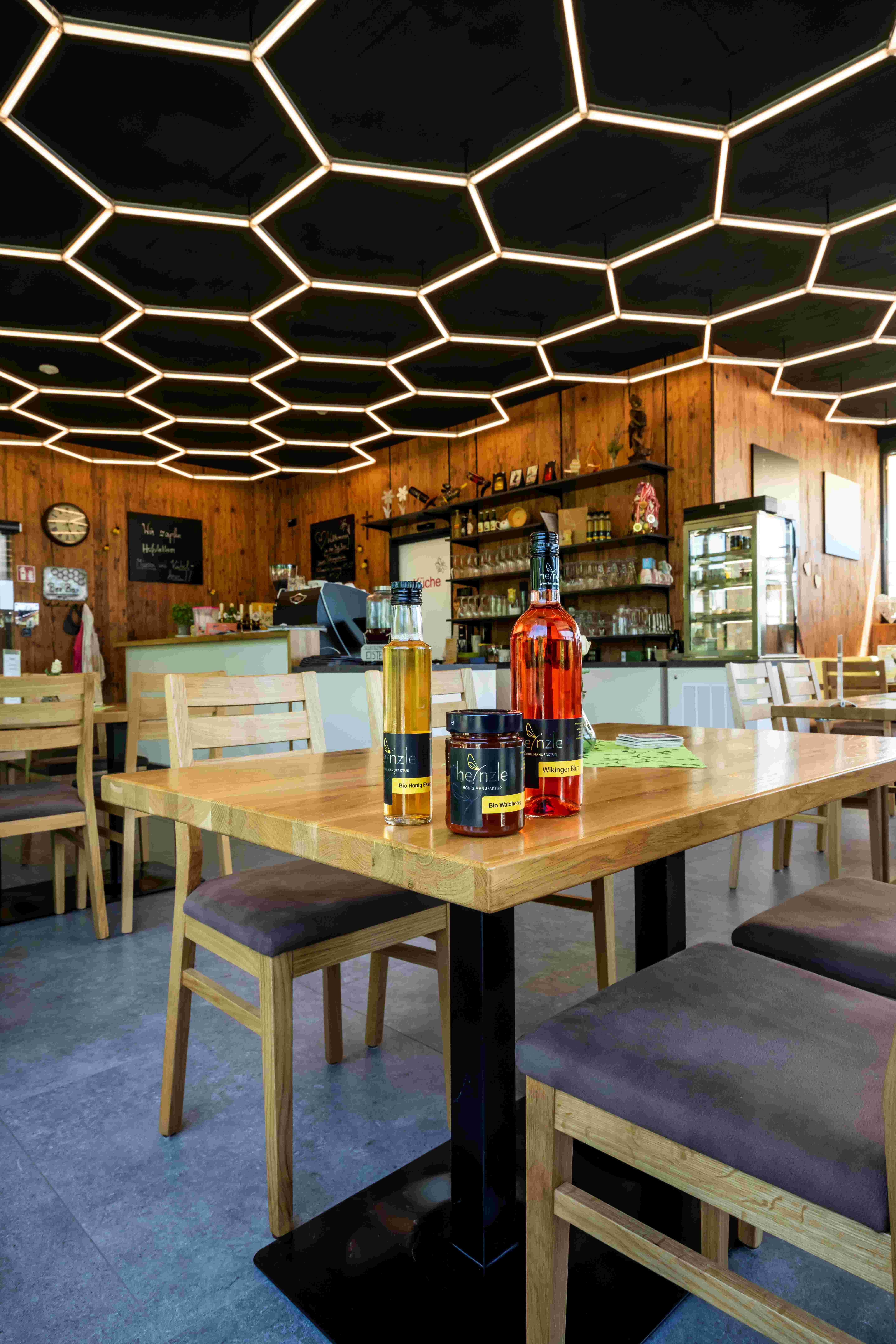 Innenansicht einer Bar mit Honigprodukten auf einem Tisch und wabenförmiger Beleuchtung an der Decke.