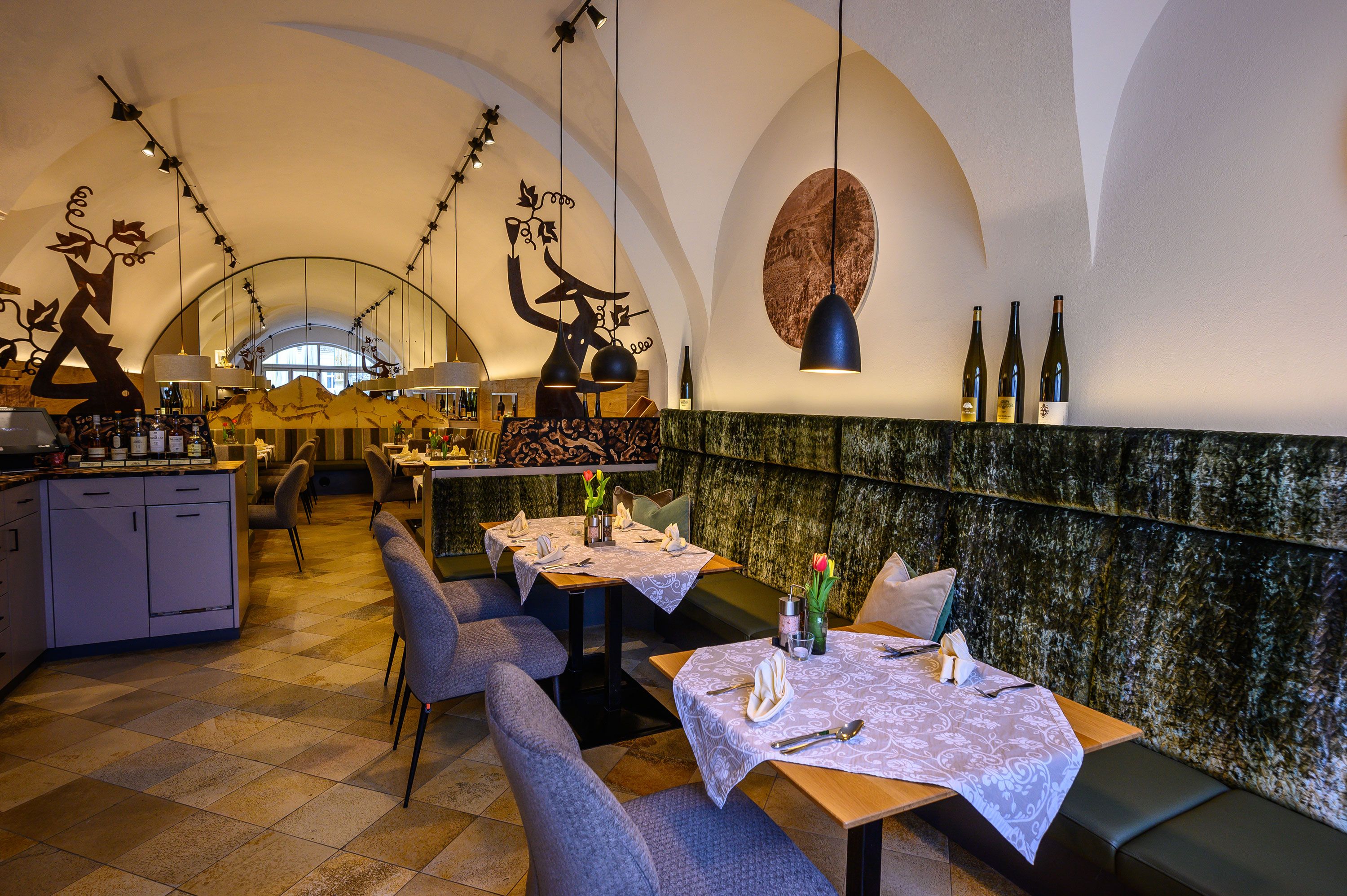 Elegantes Restaurant mit gedeckten Tischen, dekorativen Elementen und Weinflaschen auf einem Regal.