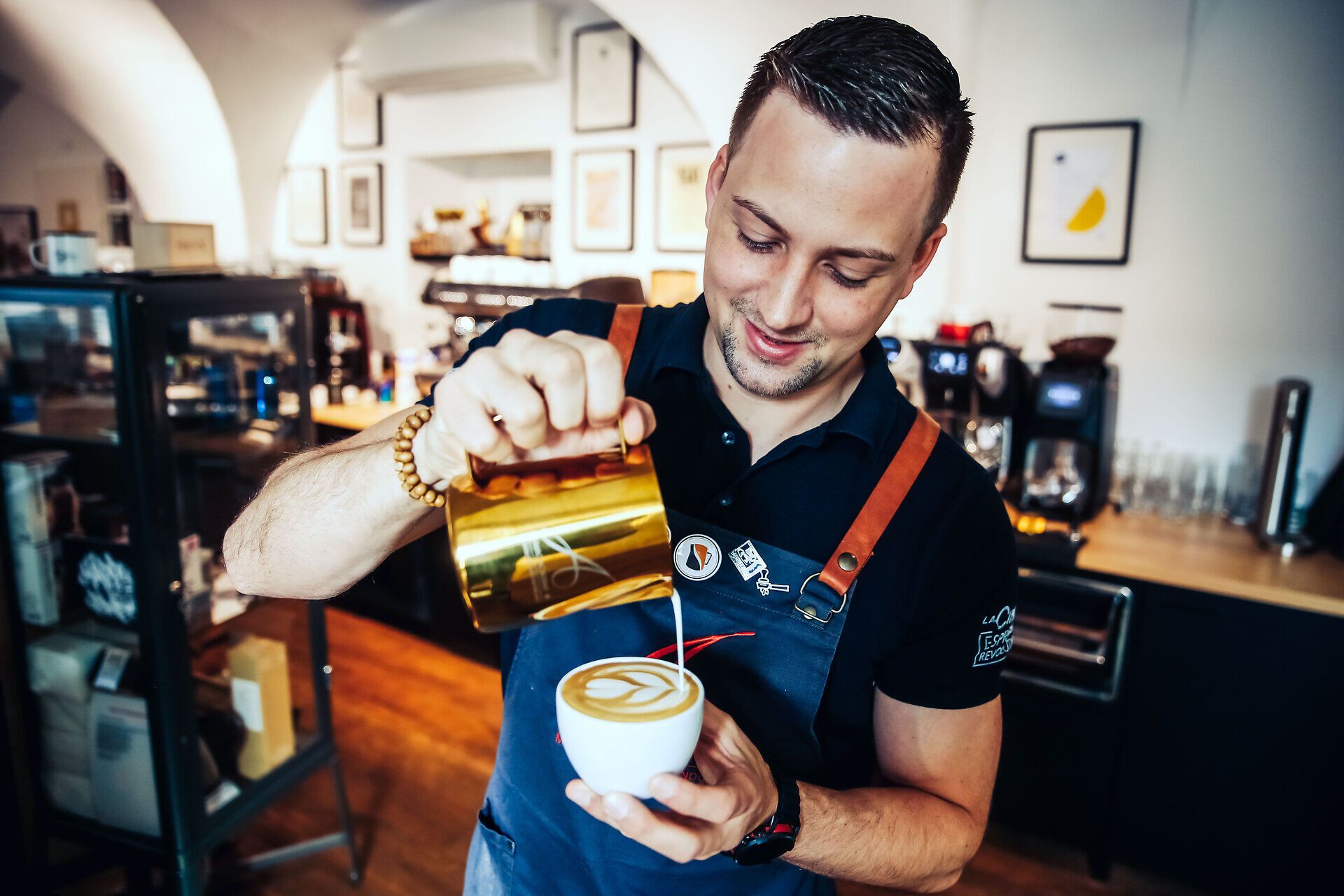 In einem einladenden Café wird mit viel Leidenschaft ein kunstvoller Cappuccino zubereitet. Der Barista lächelt, während er die cremige Milch mit geschickten Bewegungen in die Tasse gießt und ein wunderschönes Muster kreiert. Die Atmosphäre ist warm und einladend, perfekt für eine entspannte Kaffeepause.