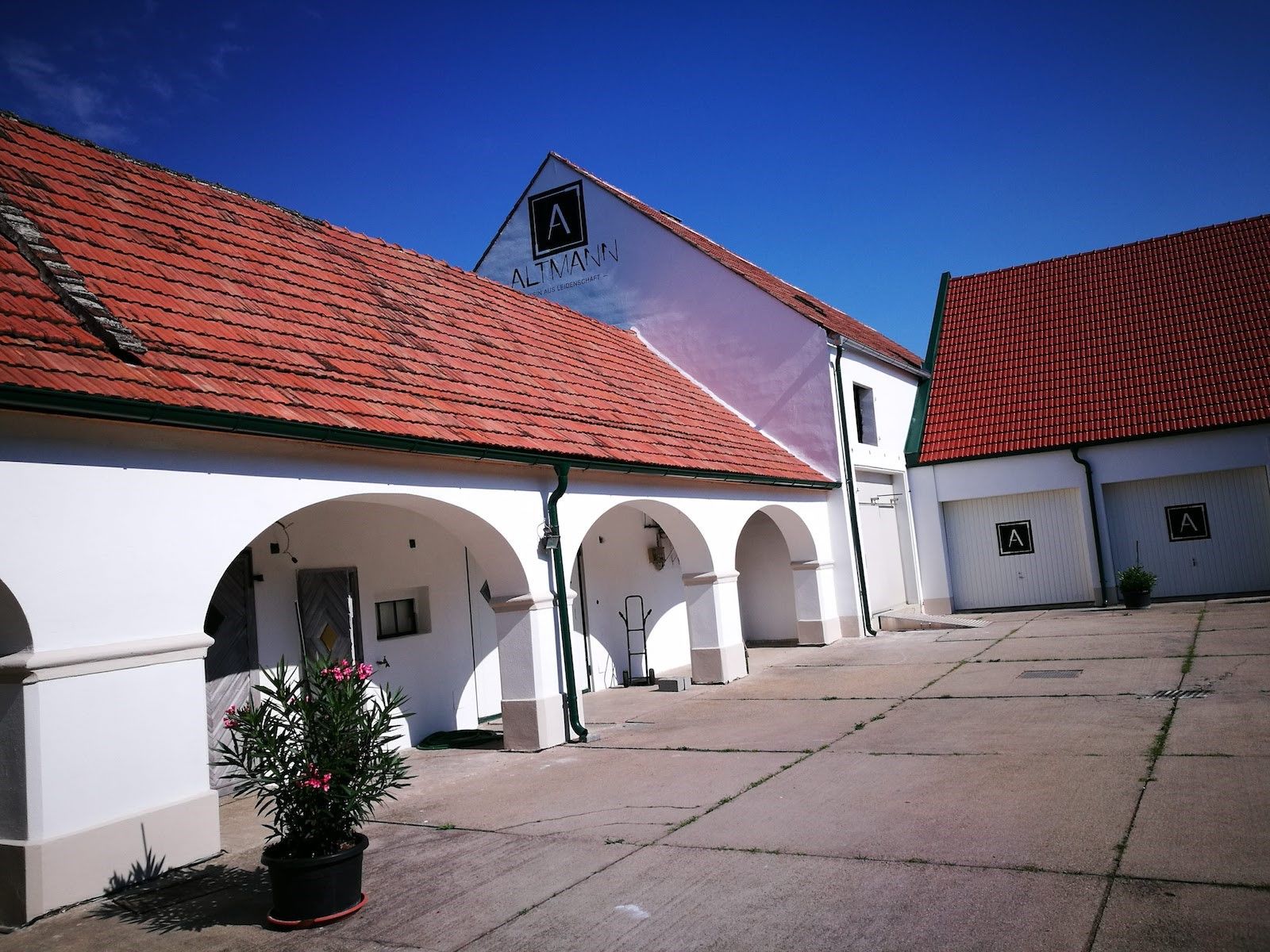 White building with red tiled roofs and arcades, blue sky.