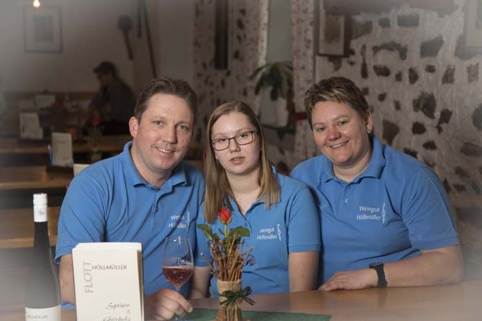 Drei Personen in blauen Hemden sitzen an einem Tisch in einem rustikalen Raum.