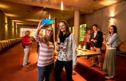 Junge Menschen stehen im Barriquekeller der Winzer Krems, wobei 2 Mädchen ein Handy hochhalten und fotografieren.