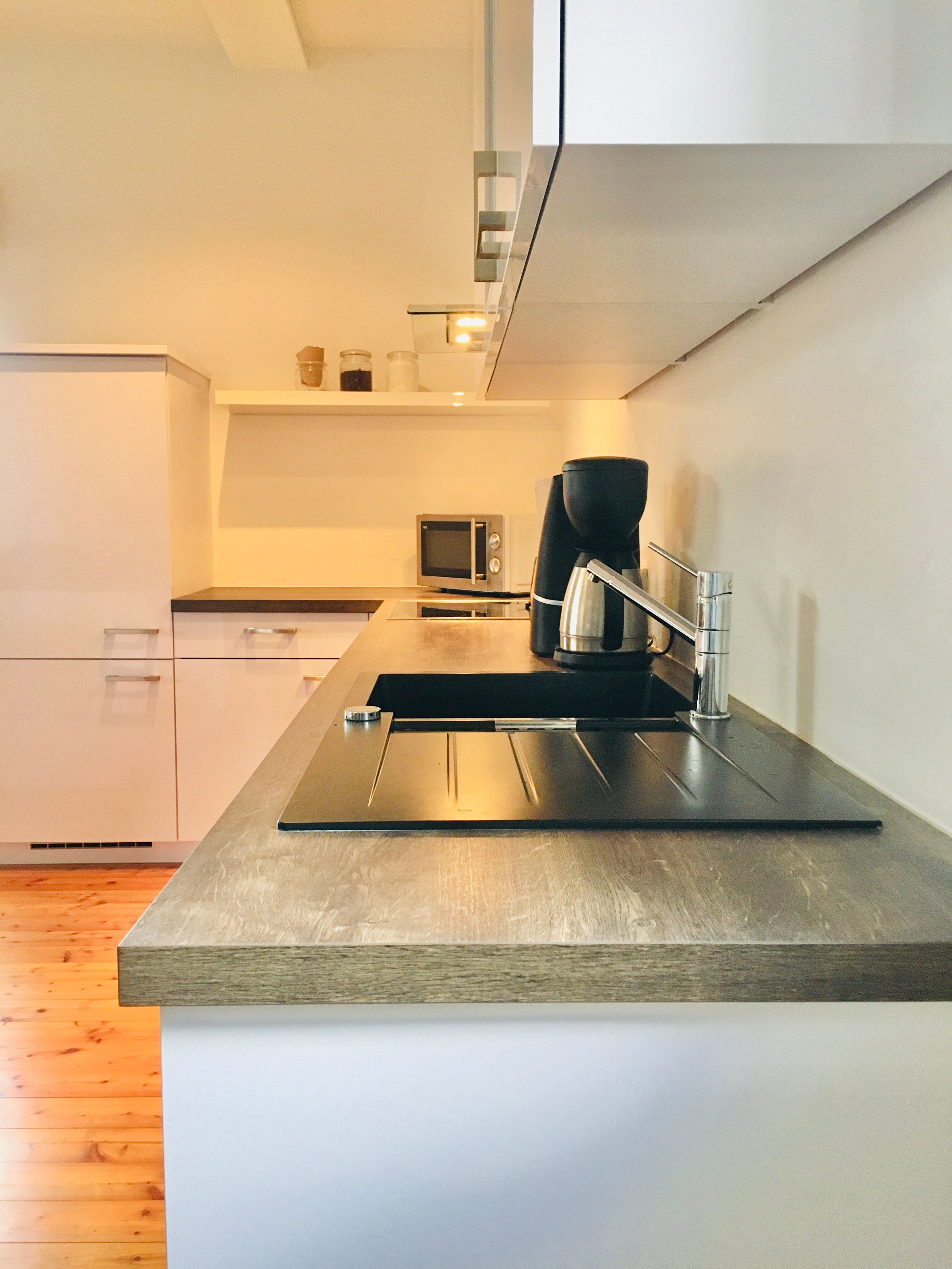 Moderne Küche mit Holzarbeitsplatte, Spüle, Kaffeemaschine und Mikrowelle.