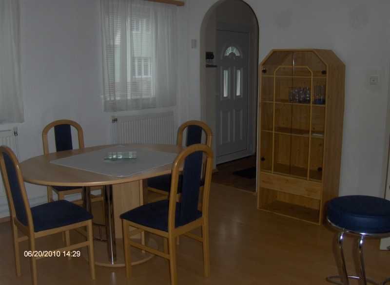 Essbereich mit rundem Tisch, vier Stühlen und einem Holzregal in einem hellen Raum.