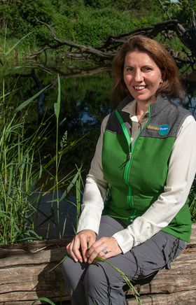 Edith Klauser, Direktorin Nationalpark Donau-Auen sitzt auf einem Baumast, im Hintergrund Wasser.