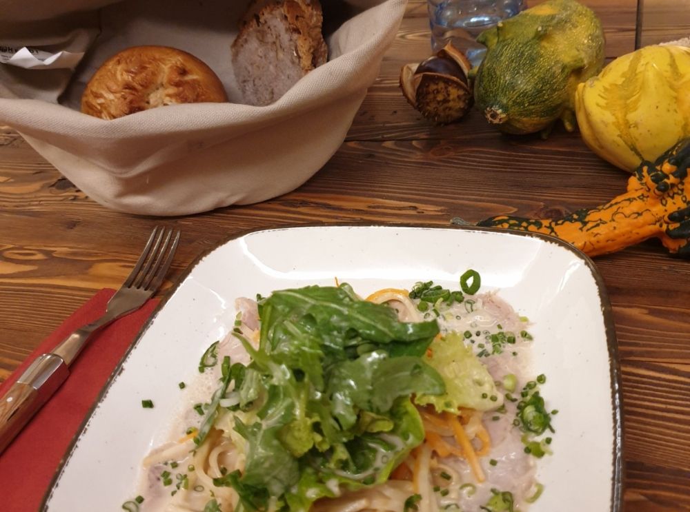 Ein Teller mit Pasta und Salat auf einem Holztisch, daneben ein Brotkorb und Zierkürbisse.