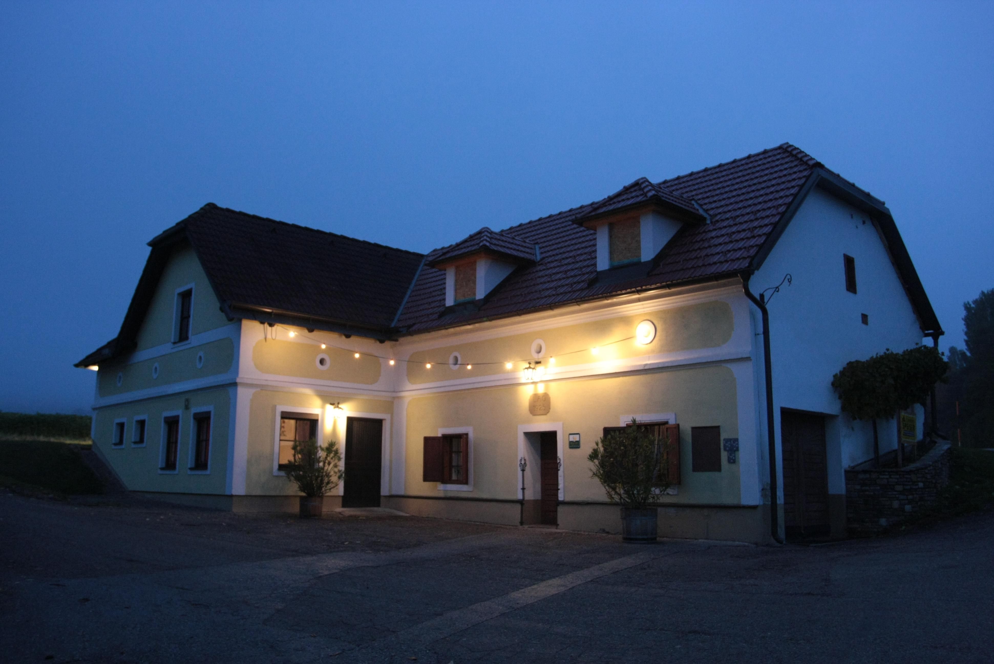 Ein traditionelles, beleuchtetes Haus mit gelber Fassade und roten Dachziegeln in der Dämmerung.